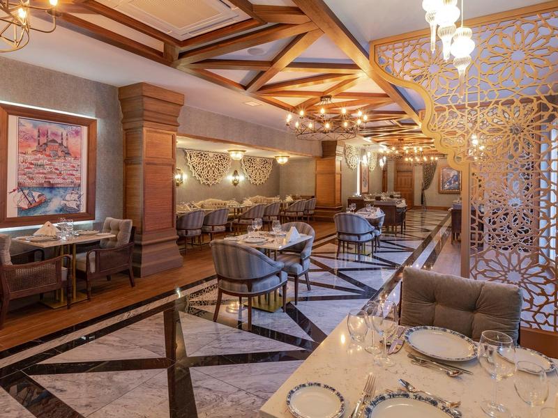 Área elegante de restaurante de hotel con mesas preparadas, techo de madera e iluminación moderna.