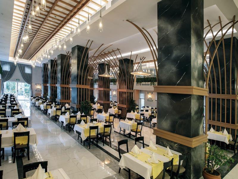 Elegante restaurante con largas filas de mesas y sillas junto a grandes columnas y techos altos.