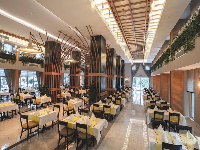 Restaurante elegante con manteles crema y columnas de madera artísticas en un espacio interior de dos pisos.