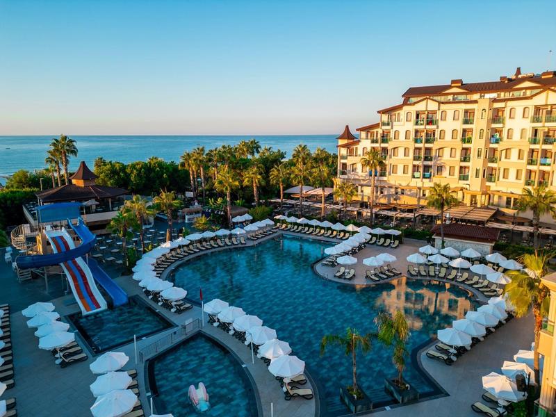 Hotel de lujo con gran piscina, tumbonas y vista al mar bajo un cielo despejado.