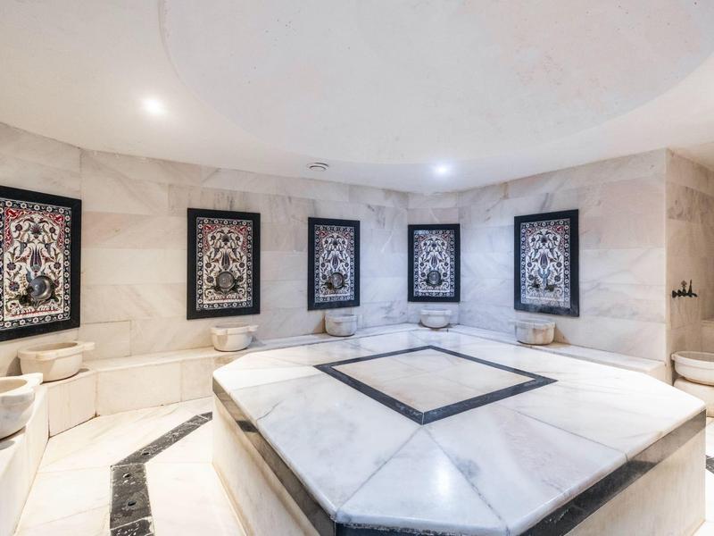 Sala de mármol blanco con azulejos y cuadros decorativos, típica de un hammam de lujo.