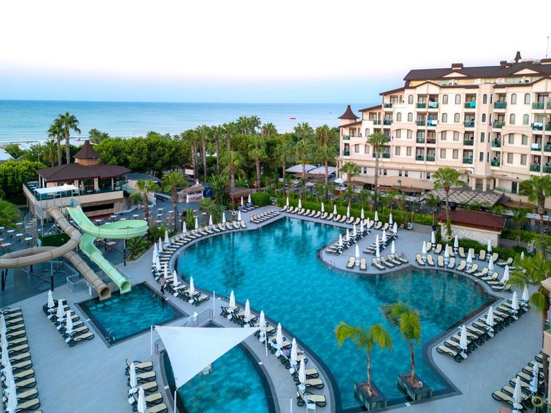 Vista aérea de un complejo hotelero con piscina grande, toboganes y sombrillas junto al mar.