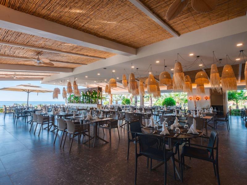 Restaurante abierto con techos de madera y numerosas mesas y sillas en un ambiente luminoso y aireado.