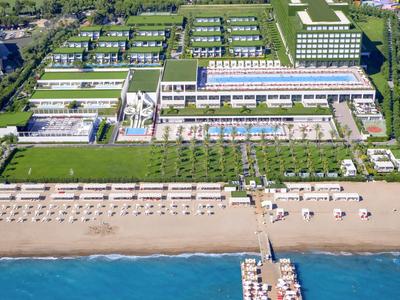 Groot hotelcomplex aan het strand met zwembaden, loungegebieden en een pier die de zee inloopt.