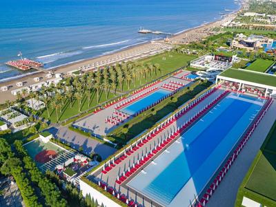 Luchtfoto van een hotel met twee buitenzwembaden, palmbomen en een strand aan zee.