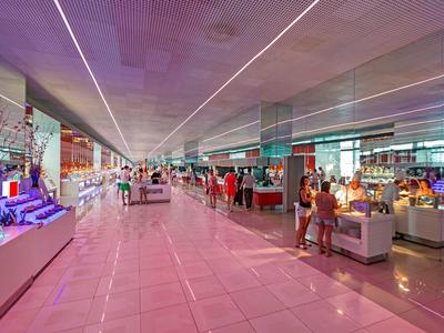 Ruime hotel lobby met glanzende vloeren, moderne verlichting en gasten bij receptie en winkels.