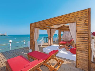 Drewniany pawilon nad morzem z czerwonymi leżakami i widokiem na niebieską wodę.