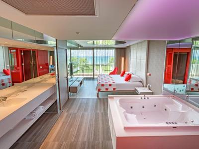 Moderne hotelkamer met jacuzzi, bed, spiegelwanden en balkon met uitzicht op groen.