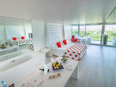 Lichte spa ruimte met bad, ligstoel, rode rozen decoraties en grote ramen met uitzicht op groen.