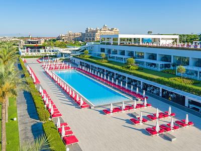 Modern hotel met groot zwembad, rode parasols en mediterrane begroeiing.