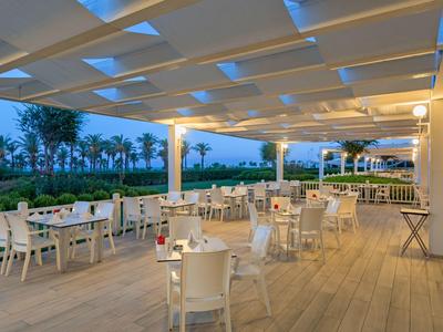 Open terras met witte tafels en stoelen onder een modern zonnescherm bij schemering.