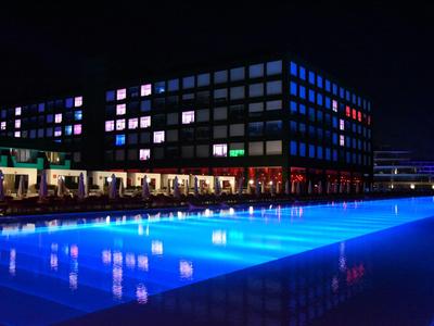 Nowoczesny hotelowy basen nocą z niebieskim oświetleniem i przylegającym budynkiem.