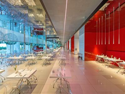 Nowoczesna restauracja ze szklanymi ścianami, czerwonymi akcentami i stylowymi stołami i krzesłami.