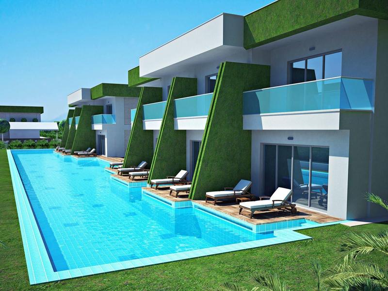 Modern hotel met een lang buitenzwembad en balkons met groene accenten onder een heldere blauwe lucht.