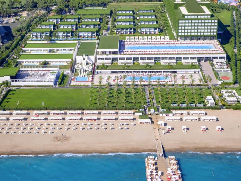 Groot hotelcomplex aan het strand met zwembaden, loungegebieden en een pier die de zee inloopt.