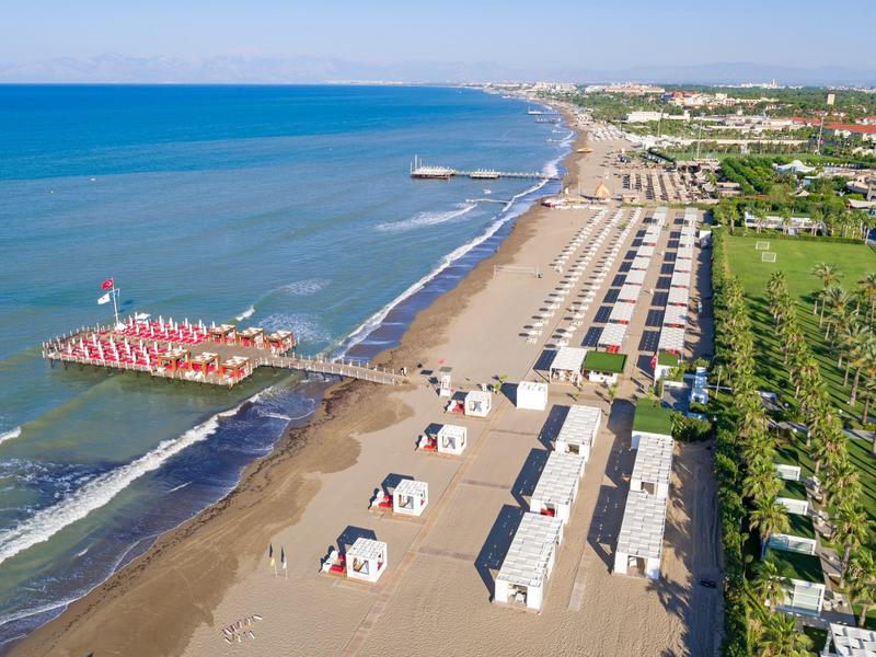 Een breed strand met rijen strandhuisjes, parasols en een helderblauwe zee die zich uitstrekt tot aan de horizon.