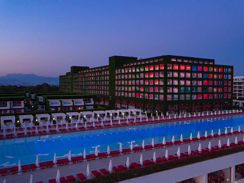 Modern hotel met levendige lichten en een lang buitenzwembad bij schemering.