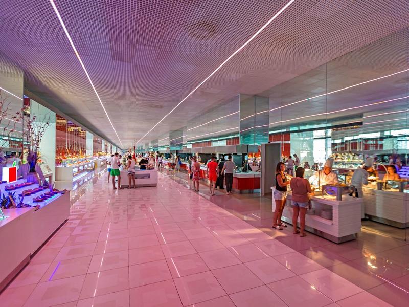 Ruime hotel lobby met glanzende vloeren, moderne verlichting en gasten bij receptie en winkels.