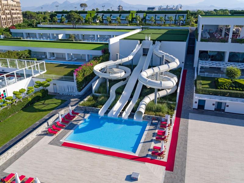 Modern hotel met groot zwembad, glijbanen en ligstoelen omgeven door groen.