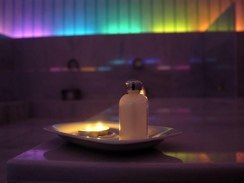 Ontspannende spa-omgeving met een kaars en rustgevende gekleurde verlichting op de achtergrond.