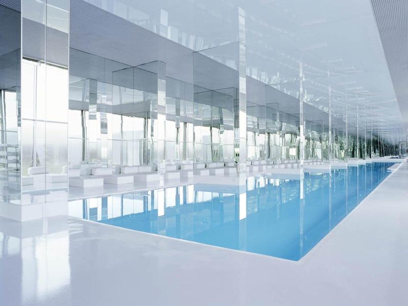 Modern binnenzwembad met reflecterende glazen wanden en strakke witte oppervlakken