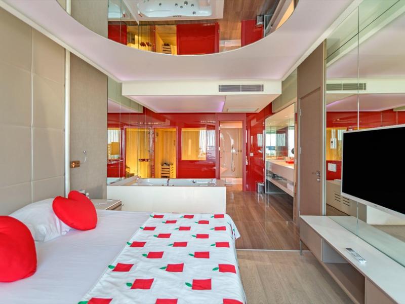 Moderne hotelkamer met hartvormige kussens, rode accenten en een groot flatscreen-tv.