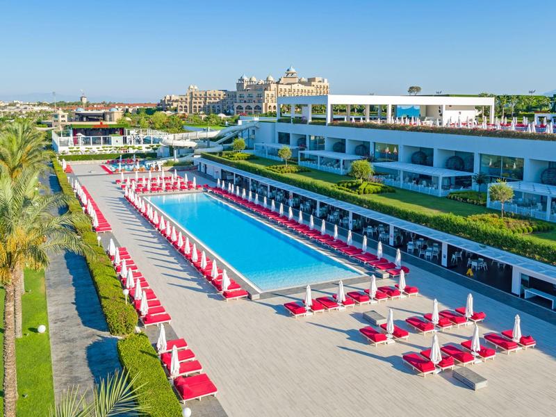 Modern hotel met groot zwembad, rode parasols en mediterrane begroeiing.