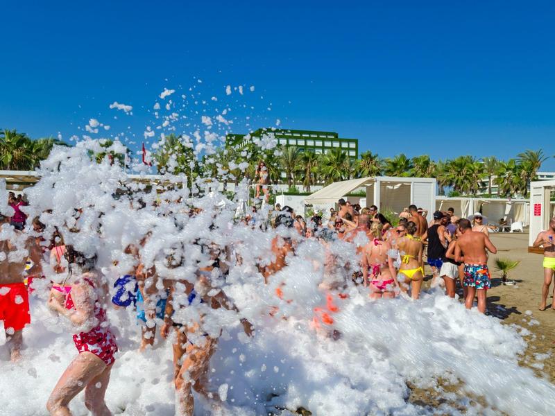 Mensen genieten van een schuimfeest op het strand bij heldere lucht en zonneschijn.