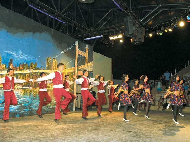 Des danseurs en costumes colorés exécutent un spectacle sur une scène avec un décor urbain.