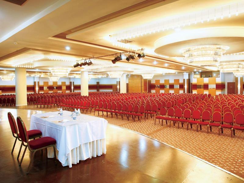 Grande salle de conférence avec des chaises rouges et une table recouverte de nappes blanches à l'avant.