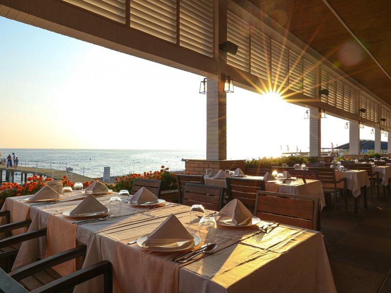 Un restaurant avec des tables dressées donnant sur la mer au coucher du soleil.