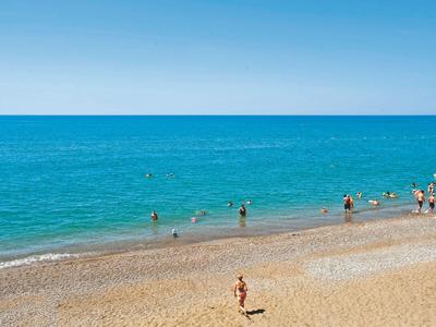 Pláž se zlatým pískem a lidmi plavajícími v čistém modrém moři.