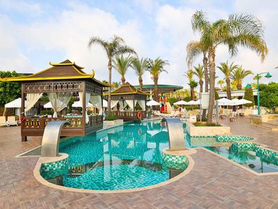 Espace piscine avec pavillon, palmiers et chaises longues sous un ciel bleu dans une station.