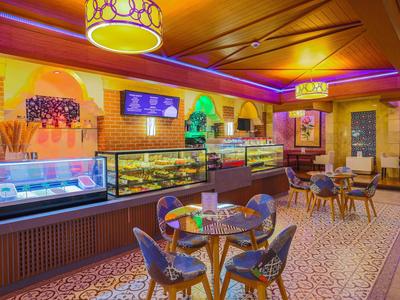 Café confortable avec éclairage chaud, vitrines de pâtisseries et sièges sur un sol décoratif.