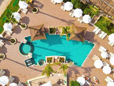 Letecký pohled na hotelový bazén obklopený lehátky a bílými slunečníky.