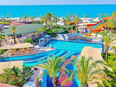 Velký hotelový bazén s vodními skluzavkami, obklopený zelenými palmami a výhledem na modré moře.