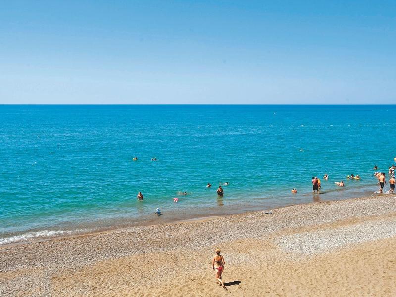 Plage avec eau bleue claire et des gens marchant et nageant au bord.