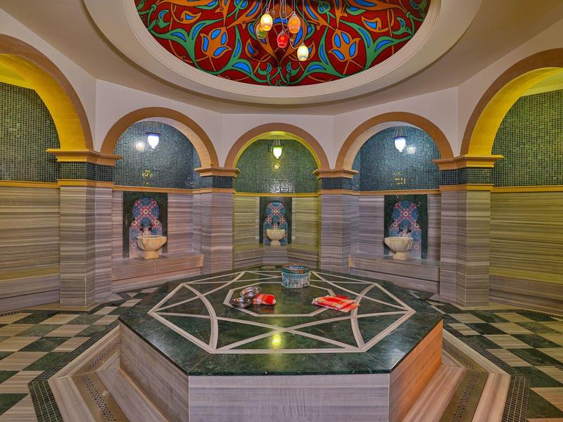 Hammam turc traditionnel avec bassin en marbre central et plafond en dôme coloré.