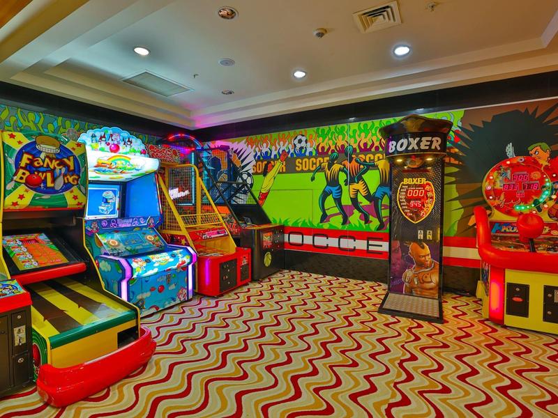 Espace de jeux coloré avec machines d'arcade et lumières néon clignotantes dans une salle de jeux d'hôtel.