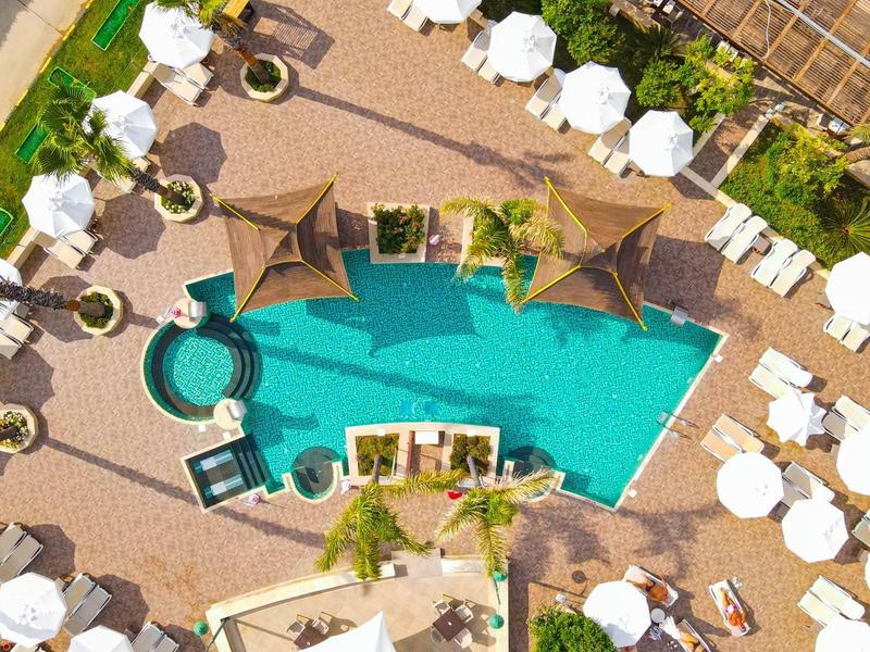 Vue aérienne d'une piscine d'hôtel entourée de parasols et de chaises longues.