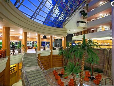 Innenraum eines modernen Gebäudes mit Glasdach, Pflanzen und Sitzbereichen in warmem Licht.