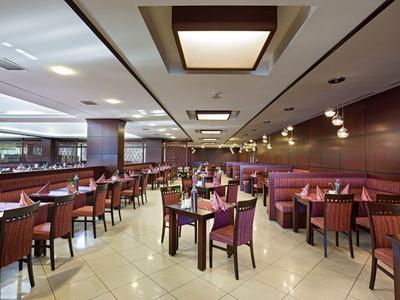 Großes, modernes Restaurant mit vielen Holzstühlen und Tischen, warmem Licht und heller Fliesenboden.