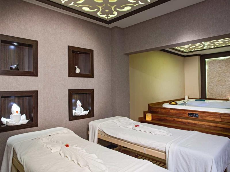 Gemütlicher Wellnessraum mit zwei Massageliegen, dekorativen Nischen und befüllter Holzwanne.