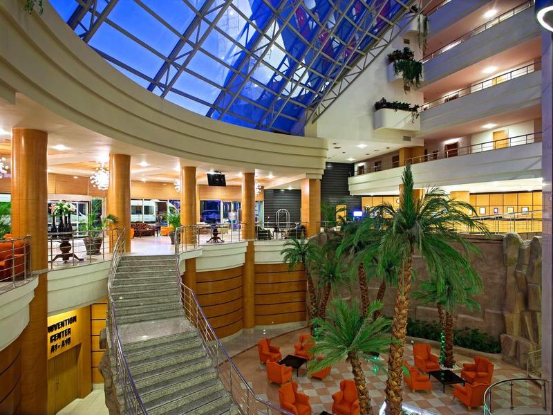 Innenraum eines modernen Gebäudes mit Glasdach, Pflanzen und Sitzbereichen in warmem Licht.