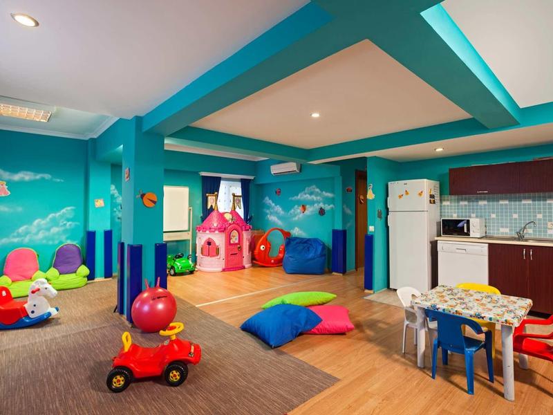 Bunter Kinderspielraum mit Spielzeug, Sitzkissen, Tischen, einer Spielecke und Küchenecke.