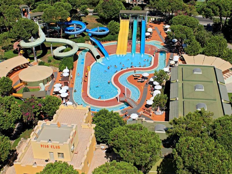 Wasserpark mit mehreren bunten Rutschen, blauem Pool und grünen Bäumen rundherum.