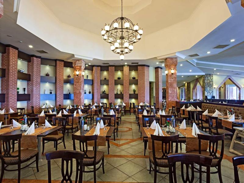 Großes Restaurant mit Holztischen, weißen Servietten und runden Kronleuchtern an der Decke.