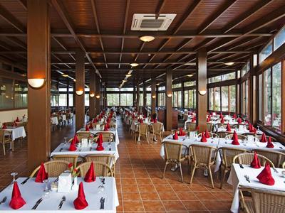 Ein großes Restaurant mit Holzbalkendecke, weißen Tischdecken und roten Servietten an den Tischen.