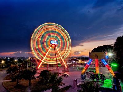 Illuminated Ferris wheel and rides at night in a waterfront amusement park