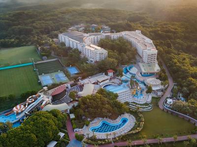 Aerial view of a resort with multiple pools and surrounding forest area at sunset.